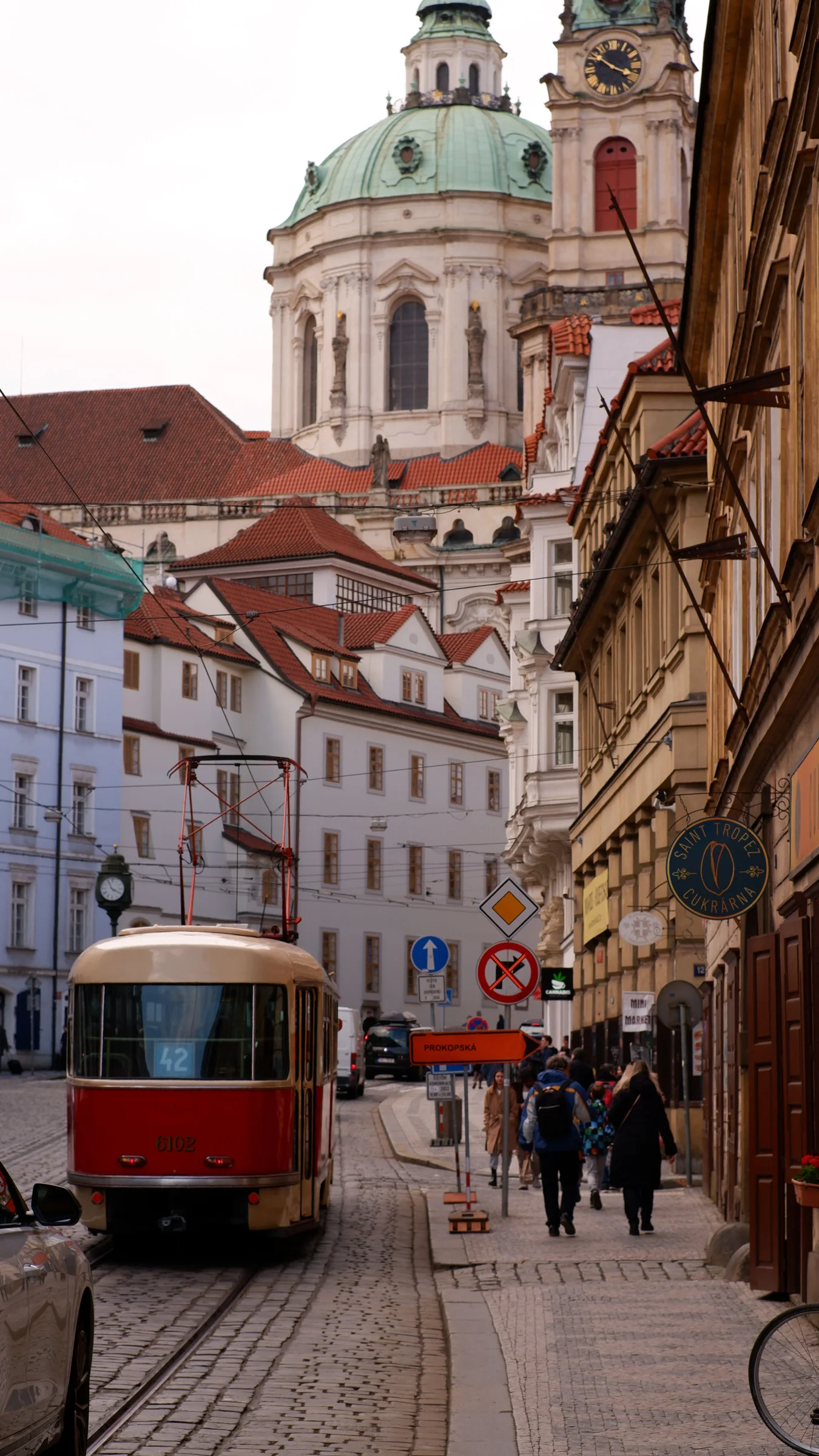 A Prague tram moving through layered architecture, signs and pedestrians