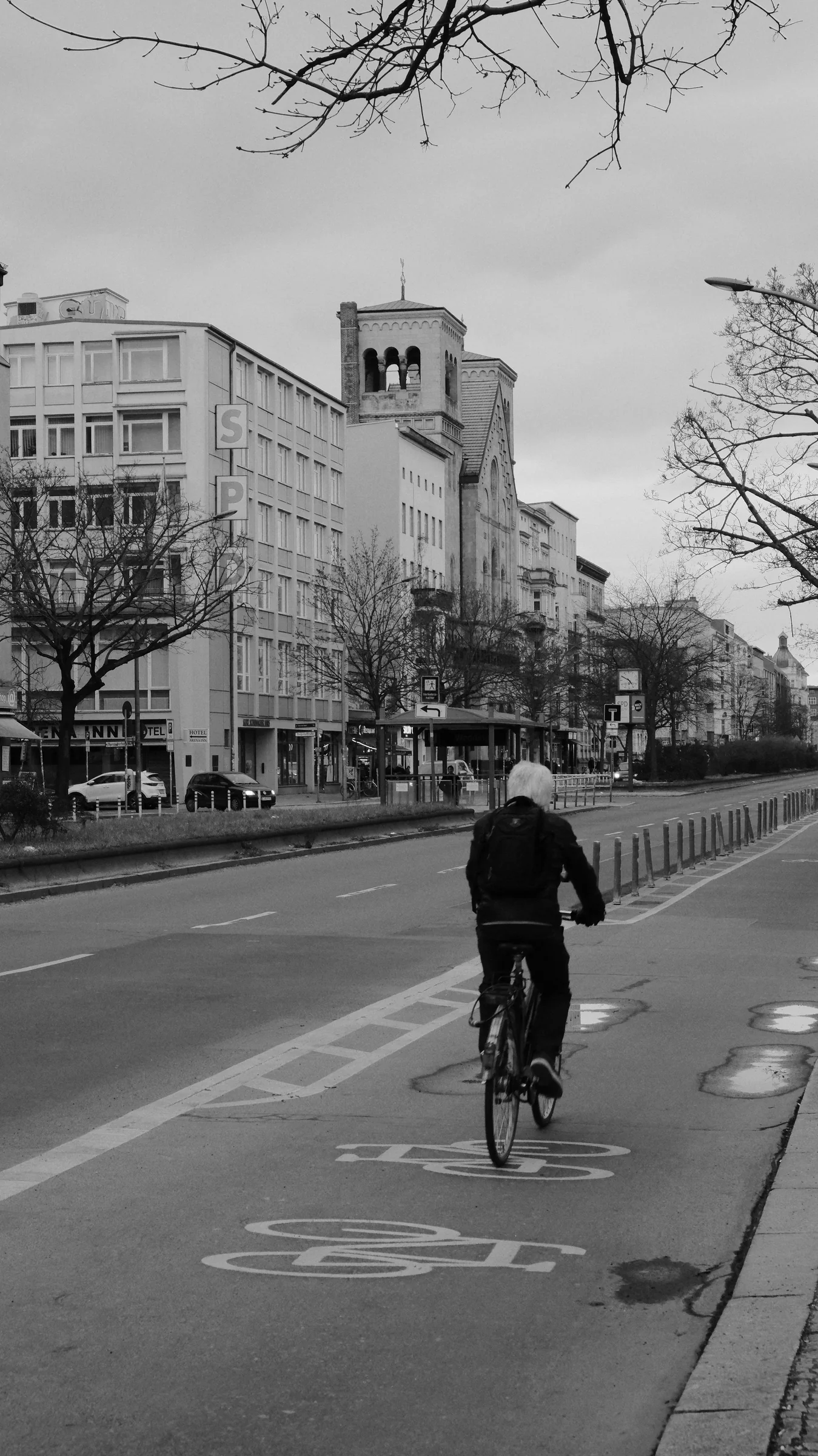A lone cyclist crossing a monochrome urban street