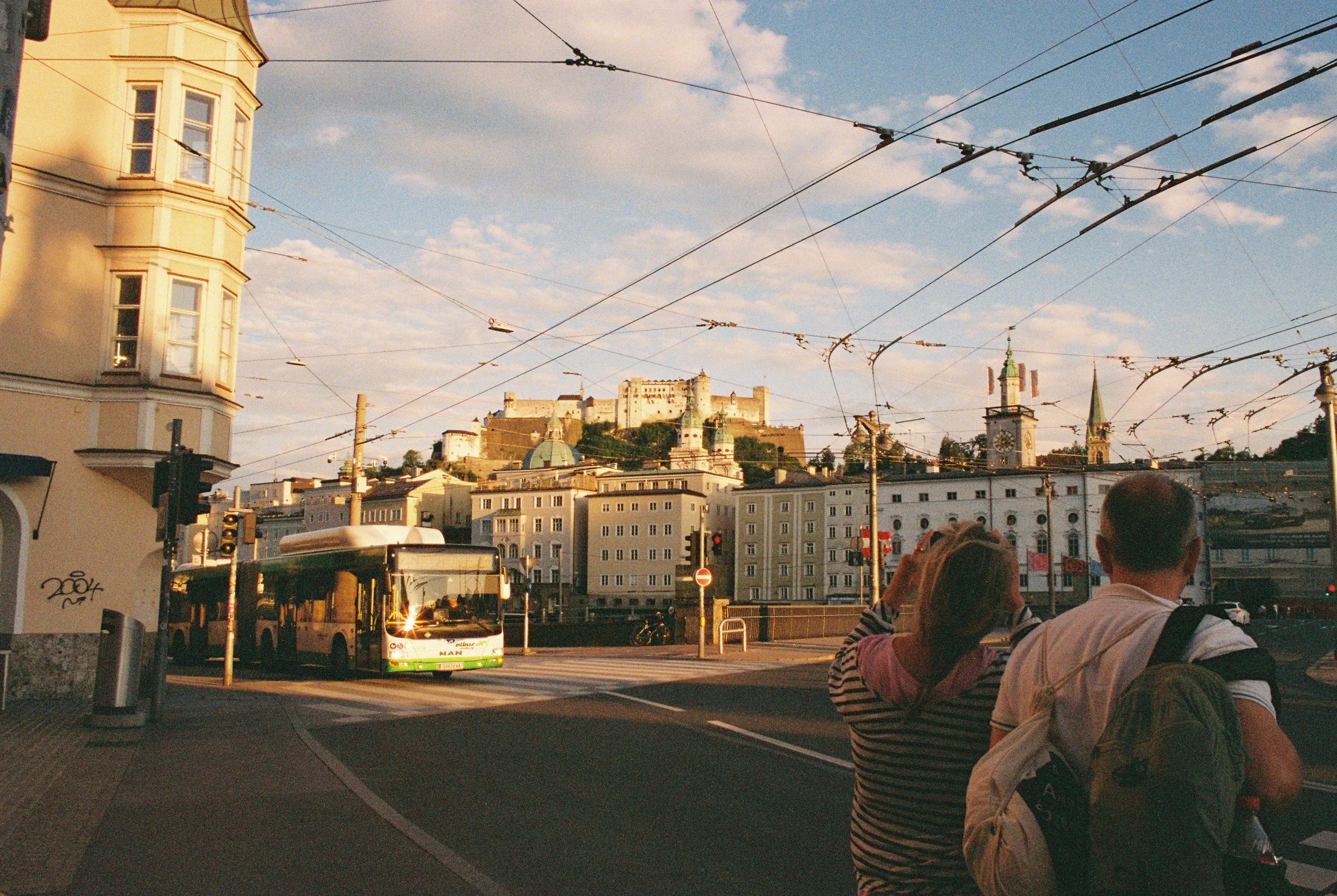 People waiting at a Salzburg intersection beneath a web of trolley wires