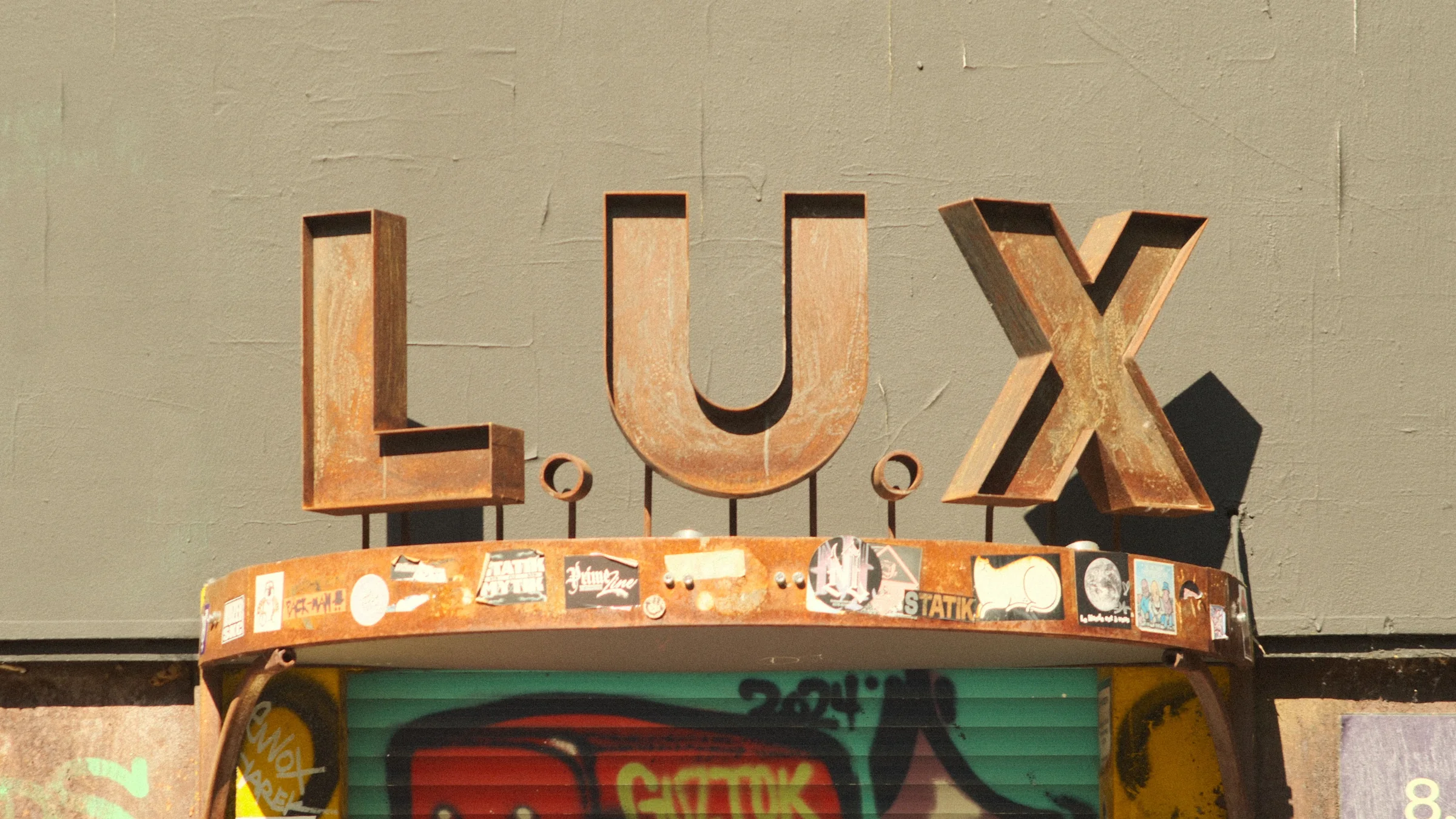 Rust-coloured LUX lettering casting a hard shadow on a textured wall