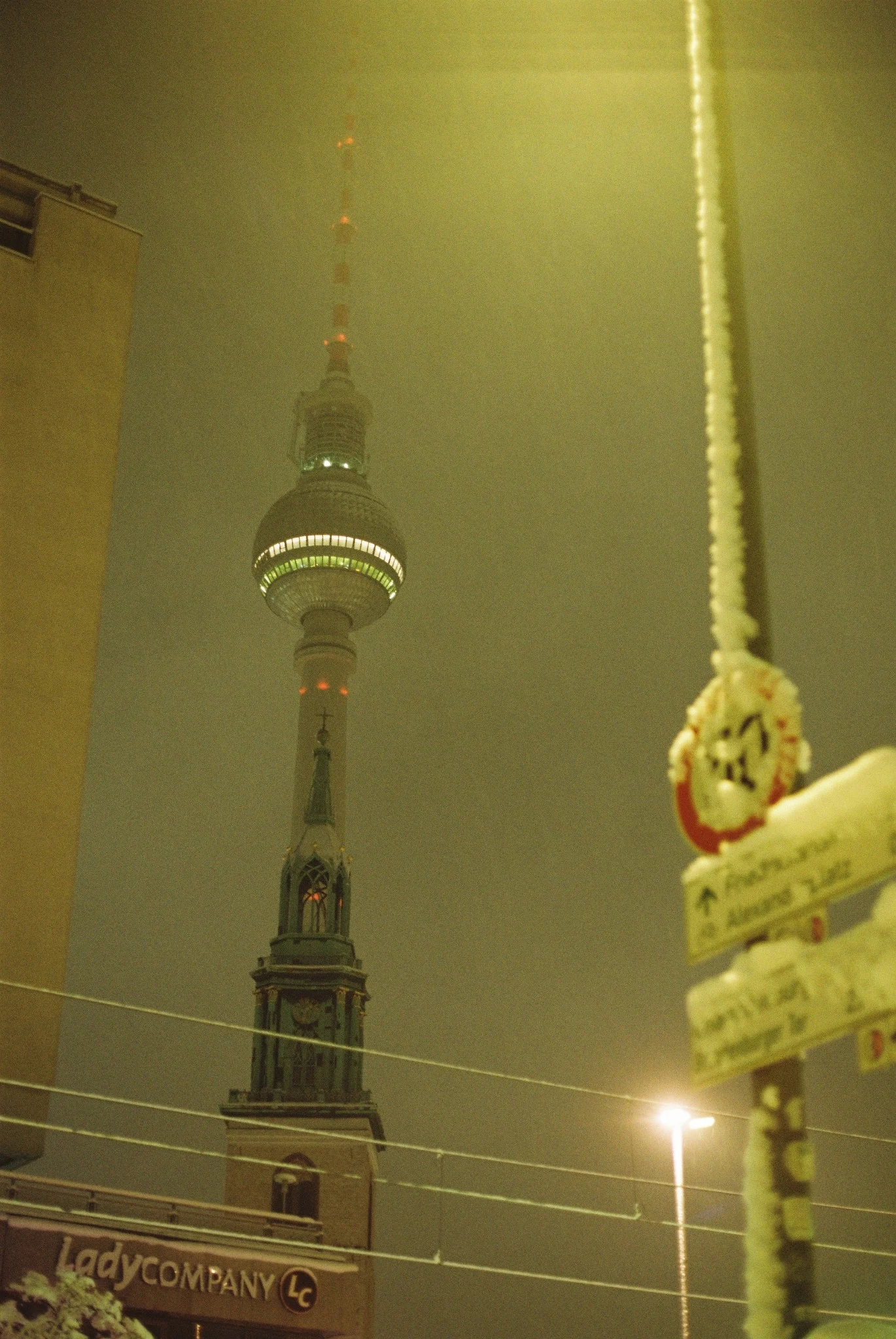 Berlin TV Tower rising above a church in yellow-green night fog, photographed on analog film