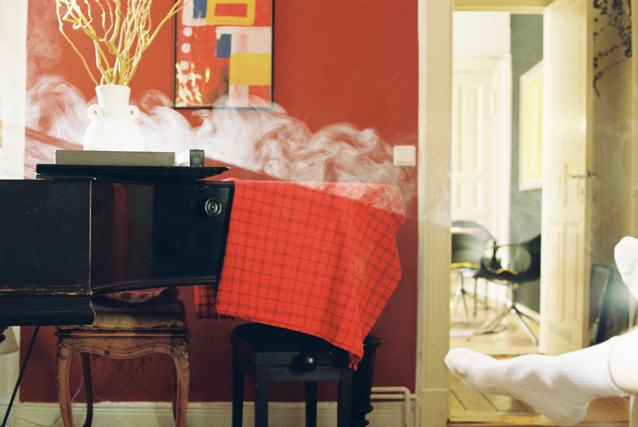 Smoke drifting through a red room with a piano and a pair of feet entering the frame