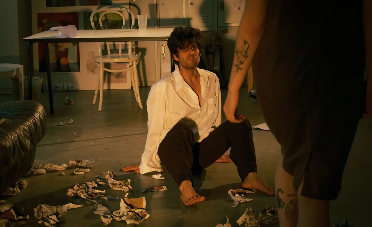 Performer seated on a stage floor during an intimate theatrical scene