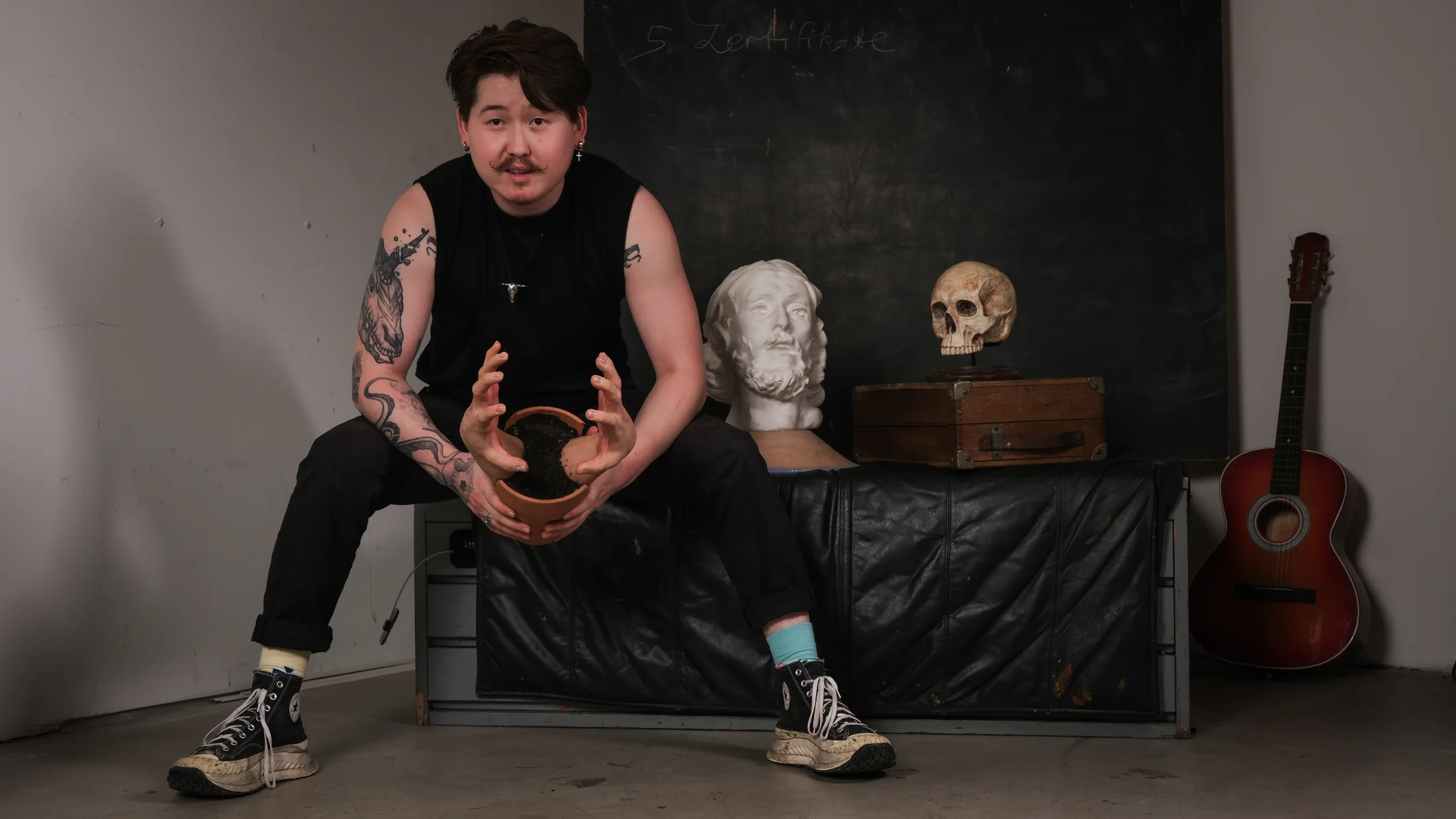 Berlin artist posing with sculptural objects, a vintage case and a guitar in a studio
