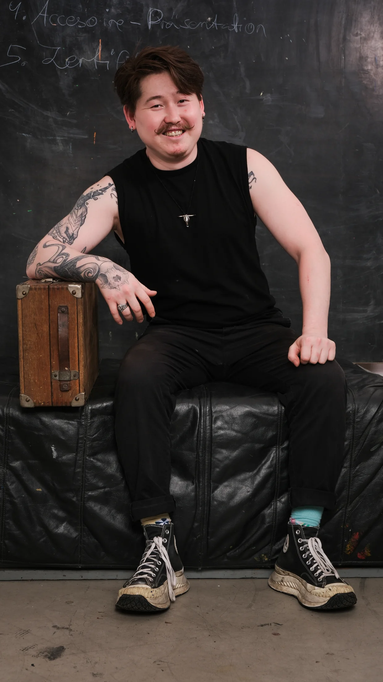 Smiling tattooed artist seated on a leather couch in a Berlin studio