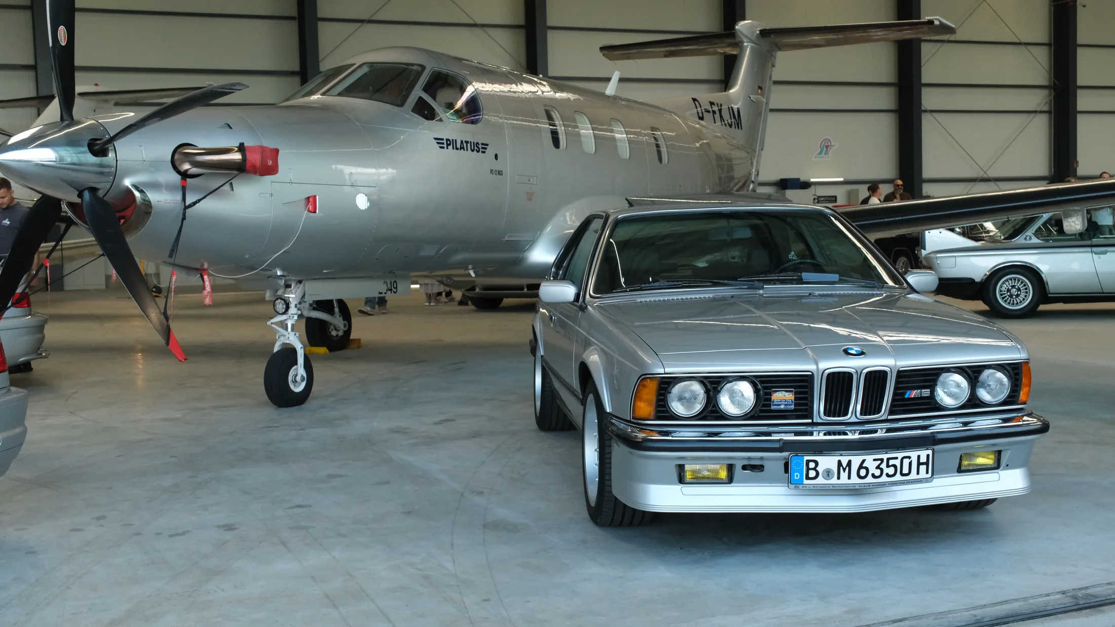 Classic BMW M6 displayed beside a Pilatus aircraft in an aviation hangar