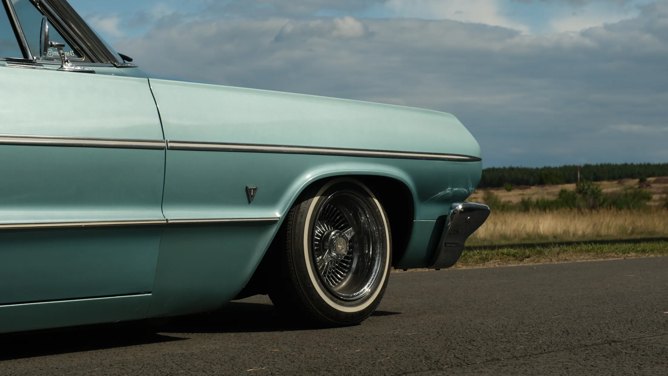 Mint green classic Chevrolet Impala body and chrome wheel photographed under an open sky