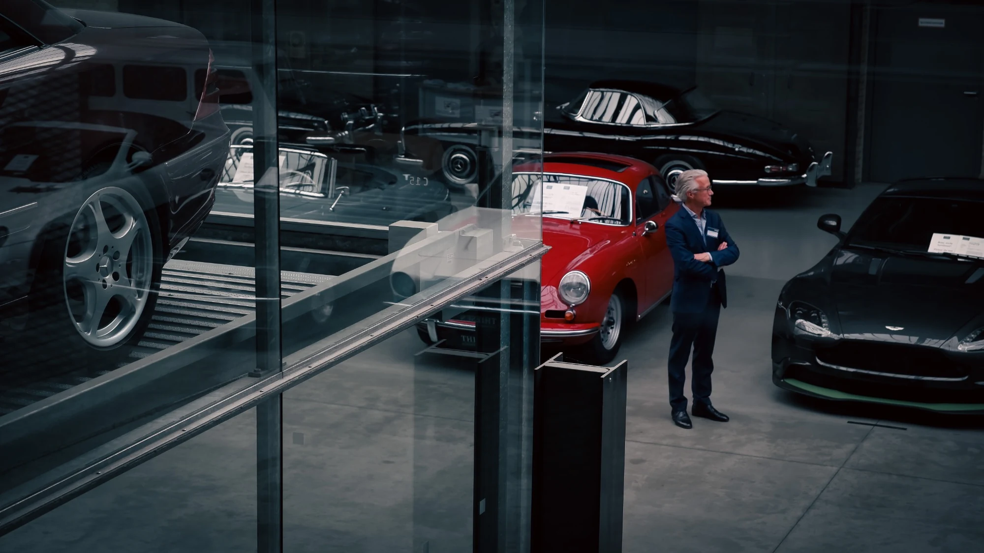 Classic cars and a curator seen through layered glass reflections in an automotive museum