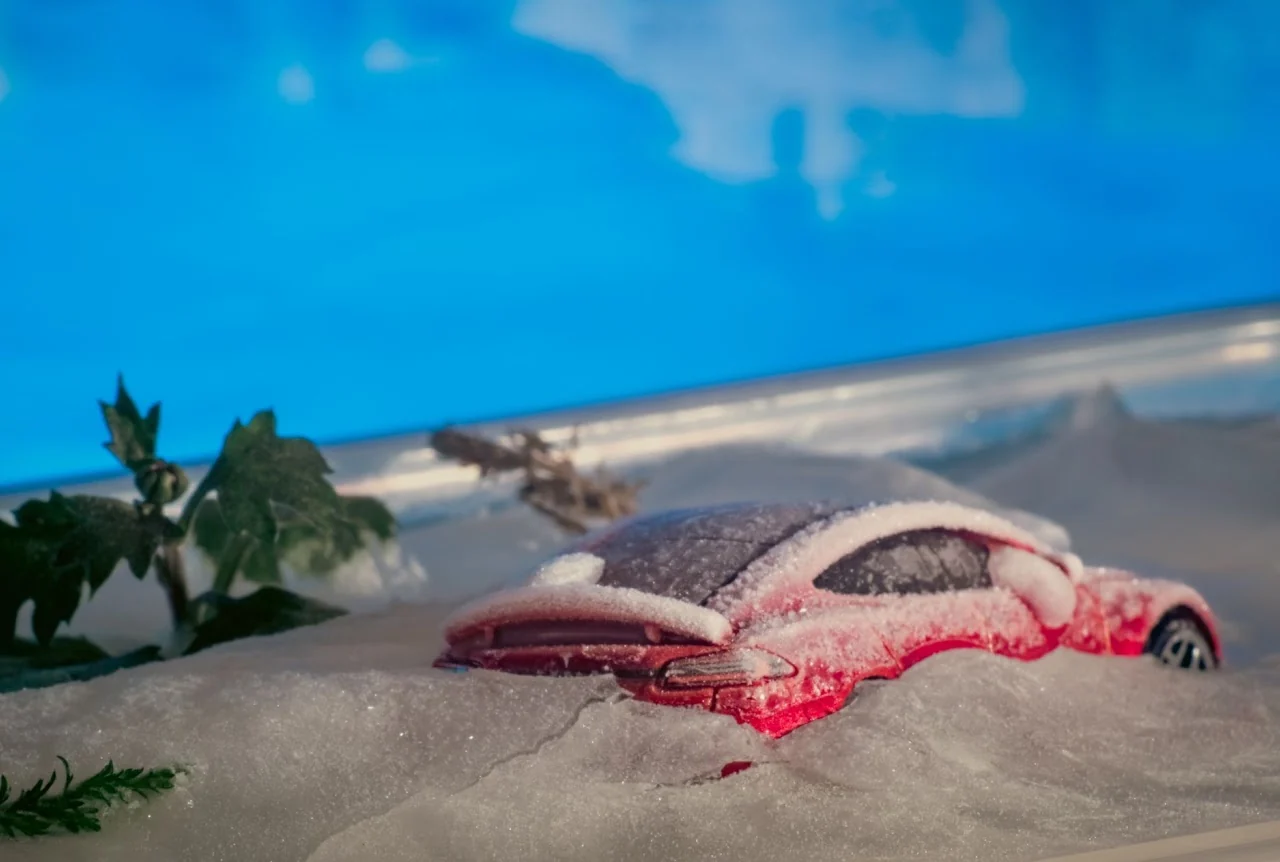 Miniature red sports car partly buried in artificial snow