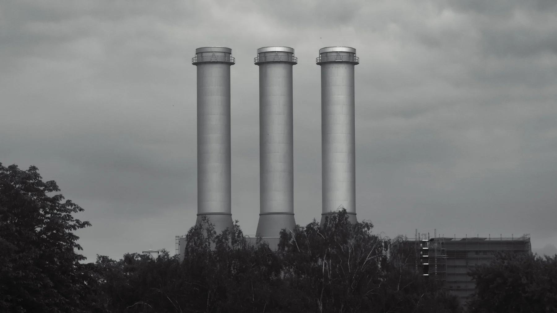 Three industrial chimneys against a dramatic cloudy sky in black and white