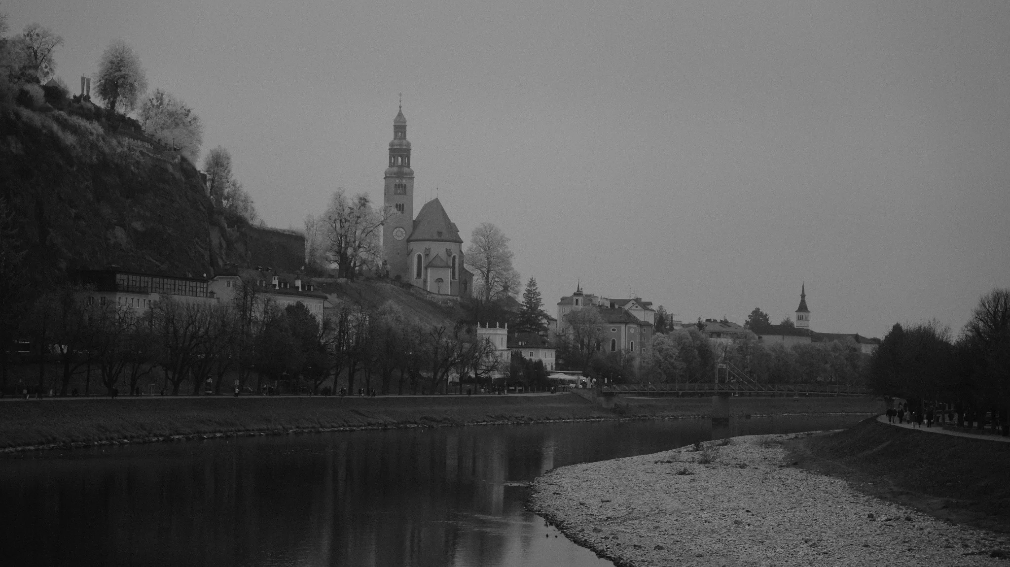 Foggy black-and-white view across the Salzach River toward the historic city and church towers