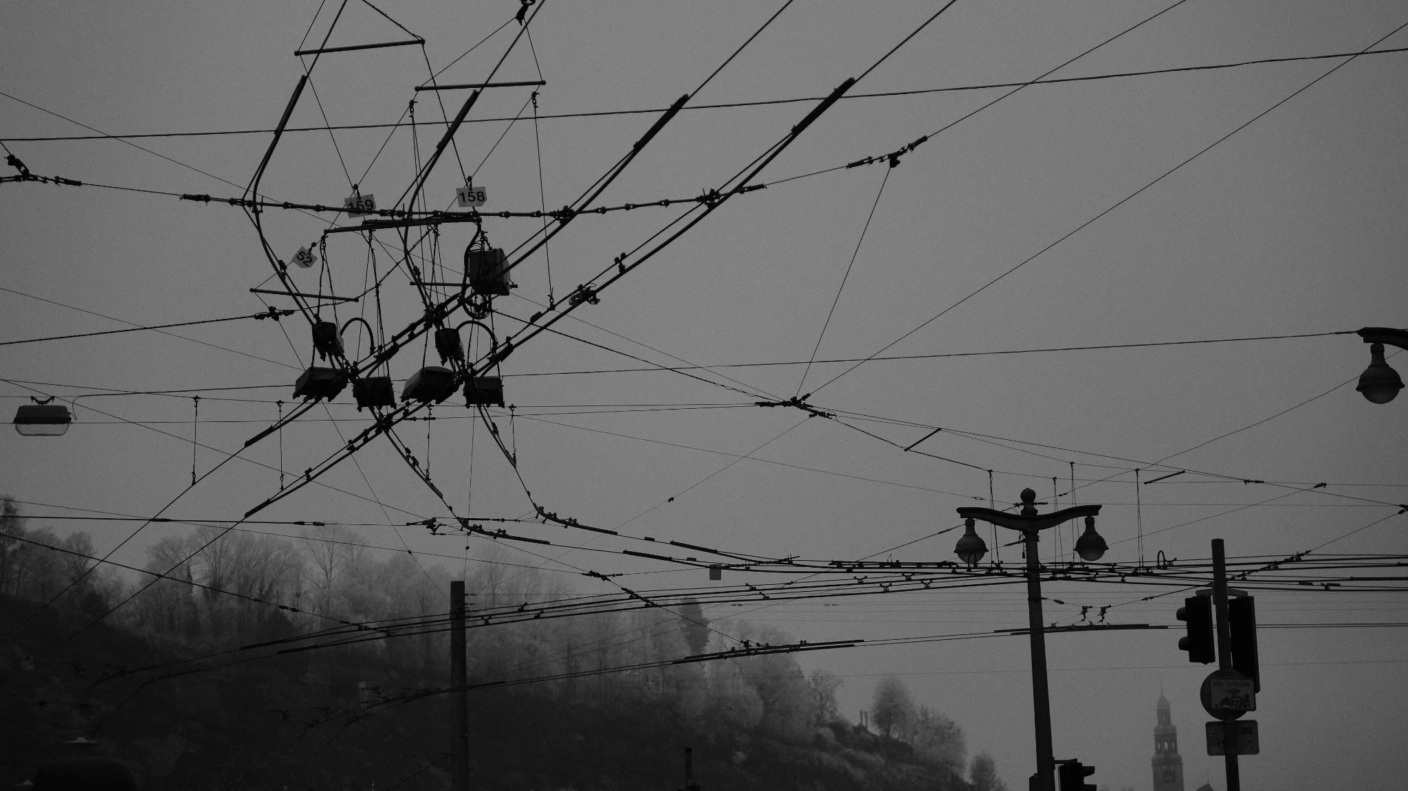Dense overhead trolleybus wires crossing a grey winter sky above Salzburg