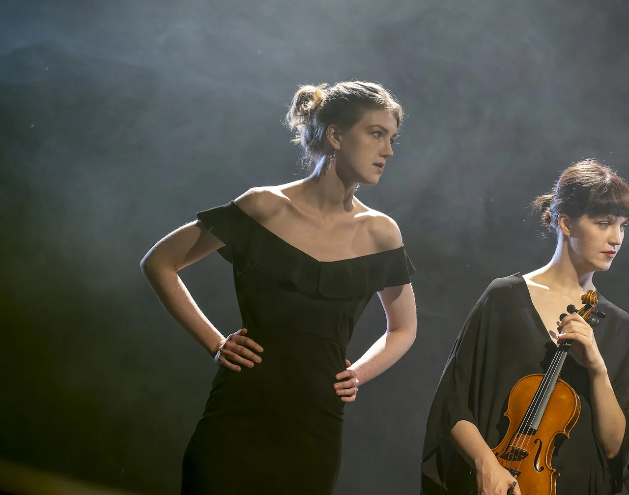 Two violinists photographed in sculptural theatre light and stage smoke