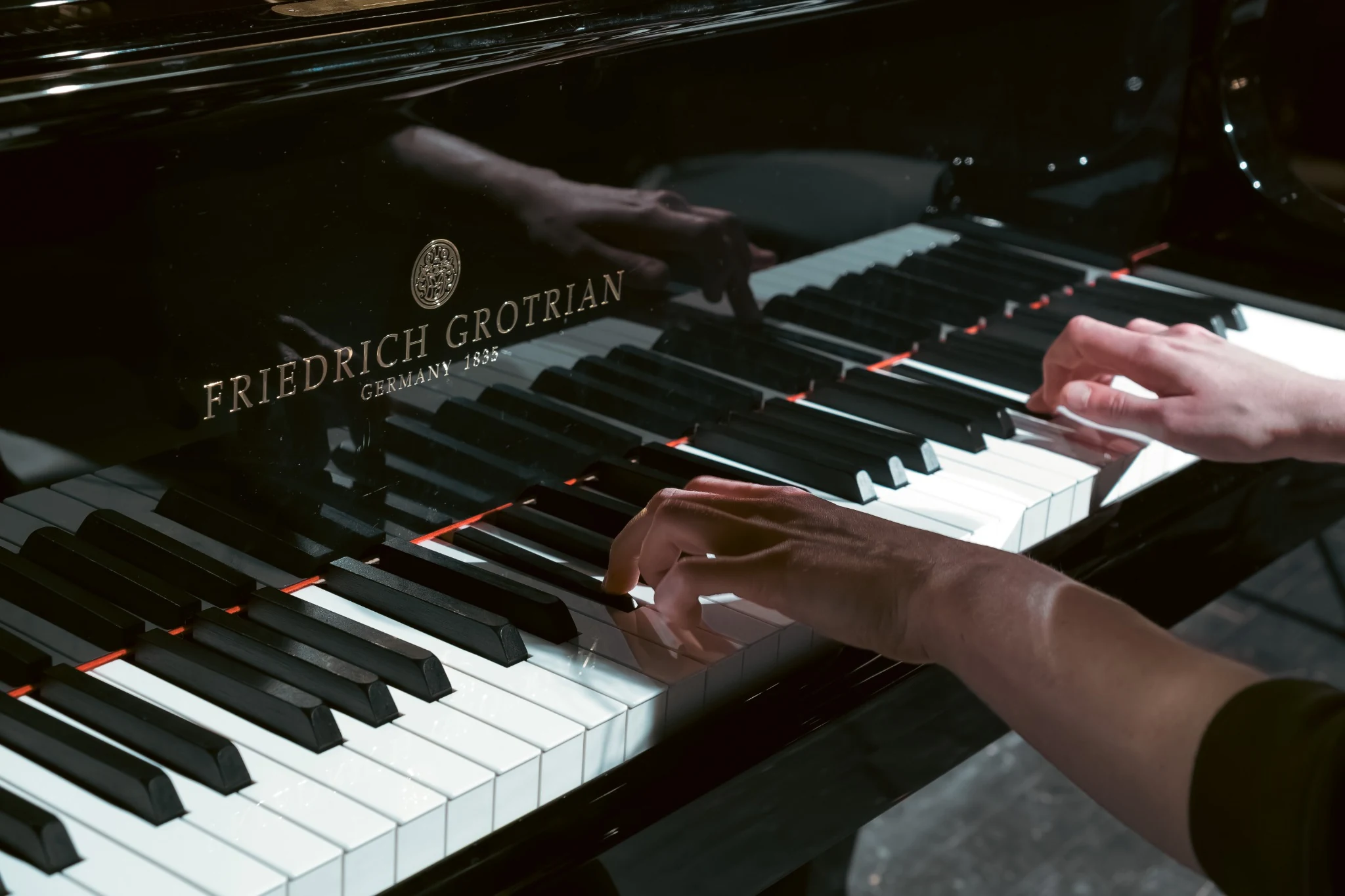 Close-up of hands playing a Friedrich Grotrian grand piano with reflections on the polished surface