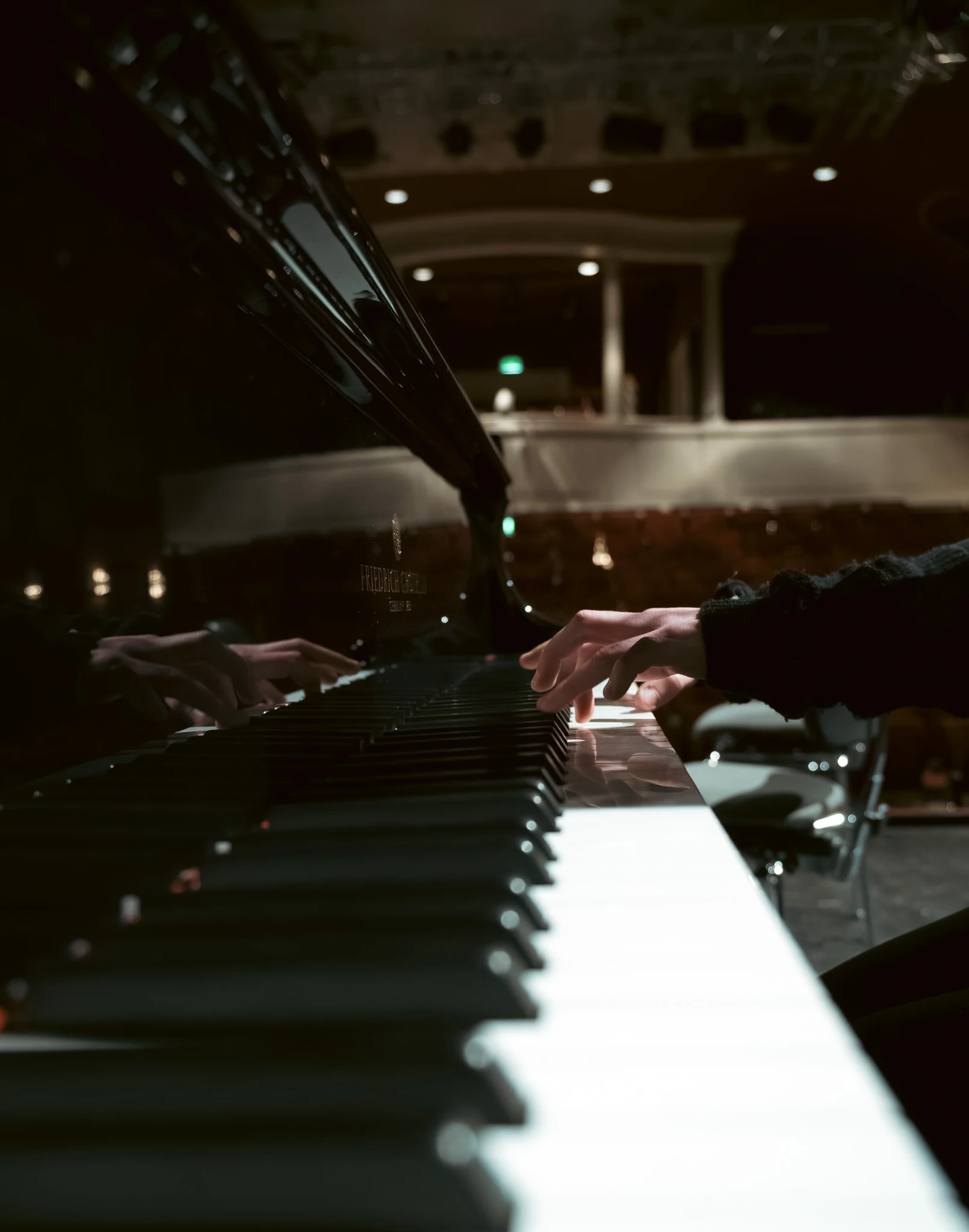 Hands playing a grand piano viewed along the keyboard toward the concert hall