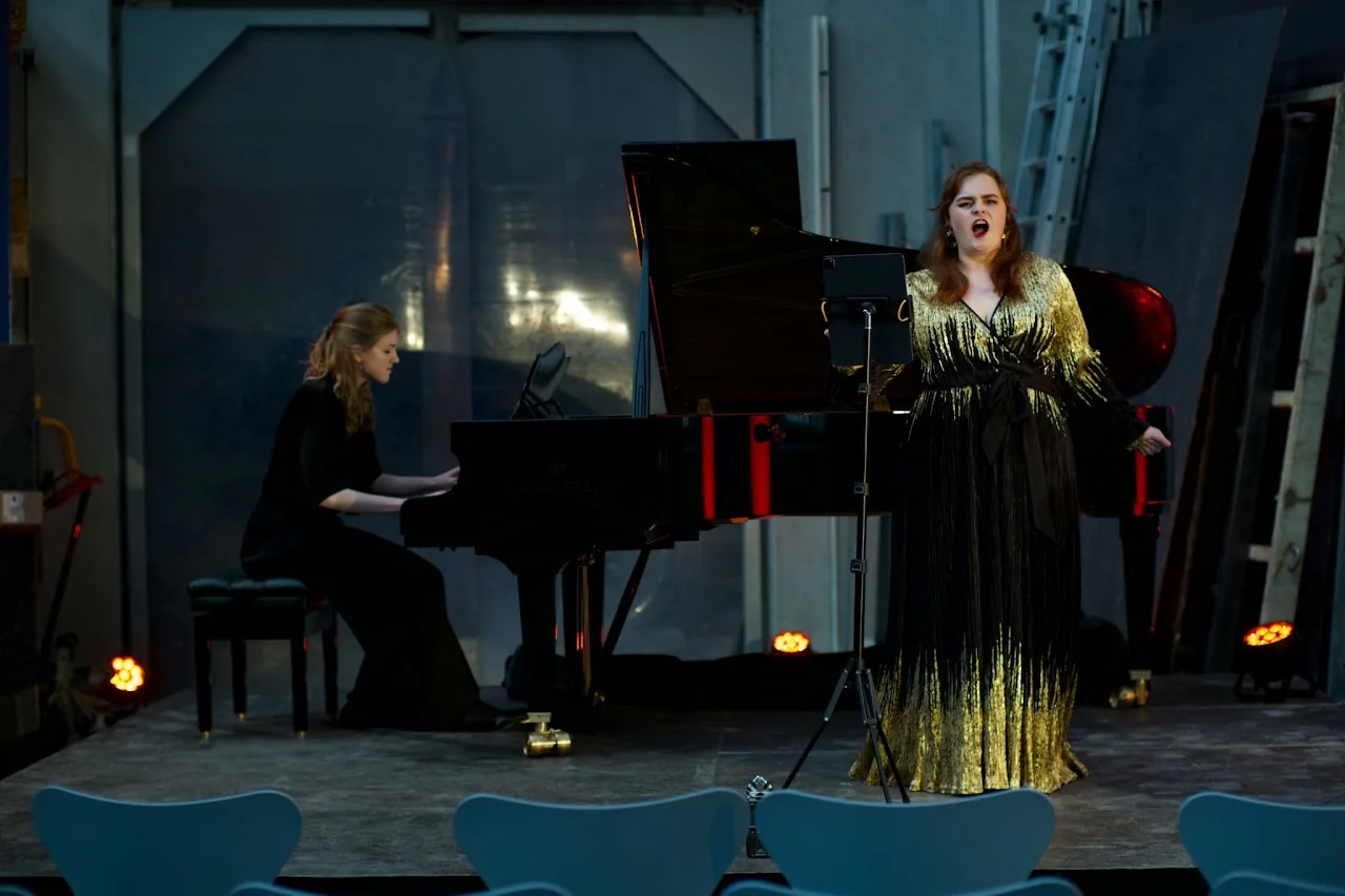 Vocalist performing beside a pianist in a dramatic concert setting