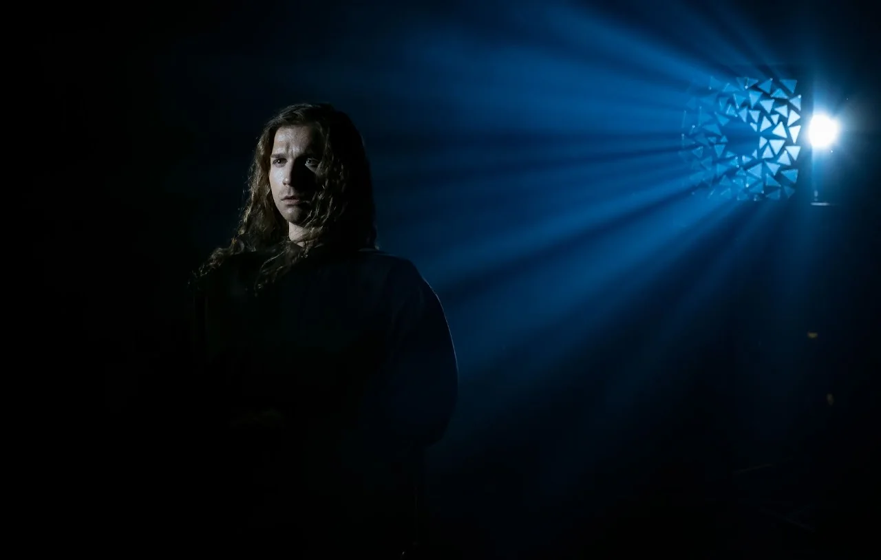 Atmospheric portrait of a singer framed by a beam of blue stage light