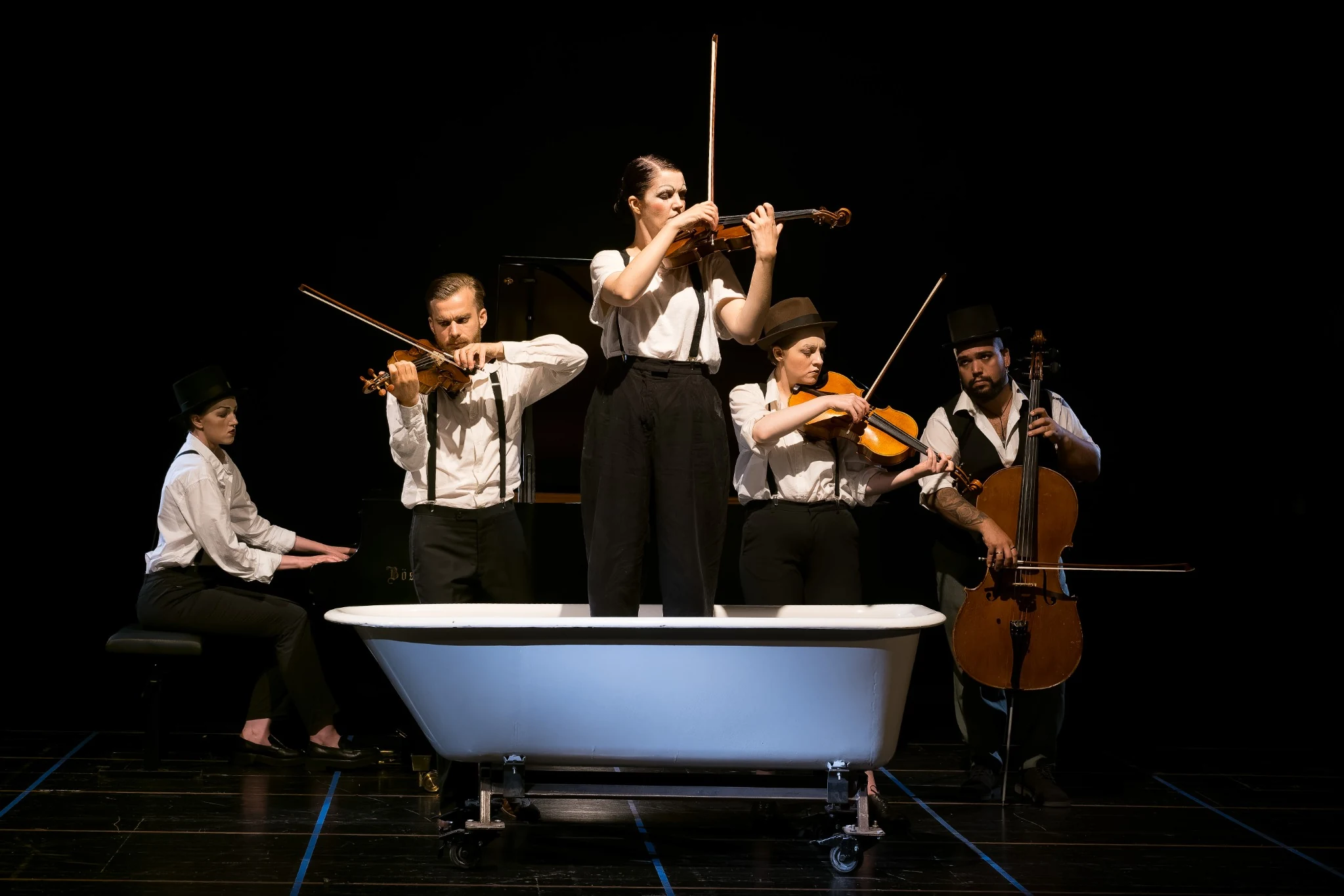 Chamber musicians performing around a bathtub in a theatrical stage production