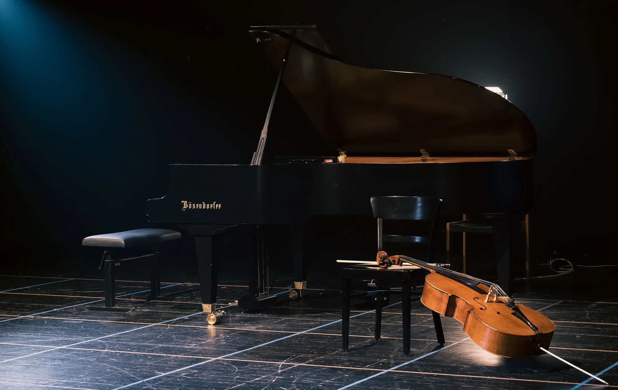 Grand piano and cello waiting on a dark concert stage